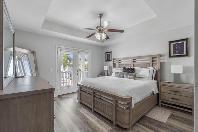 bedroom with hardwood / wood-style flooring, french doors, access to outside, a tray ceiling, and ceiling fan