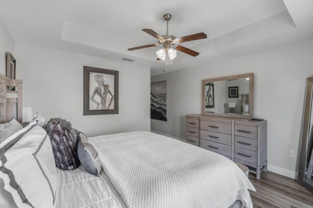 bedroom featuring ceiling fan, a tray ceiling, and wood-type flooring