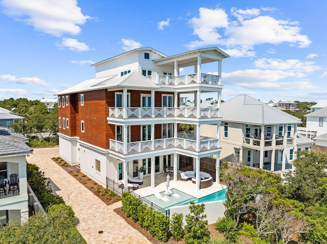 back of house with decorative driveway, a patio area, metal roof, a balcony, and an outdoor living space