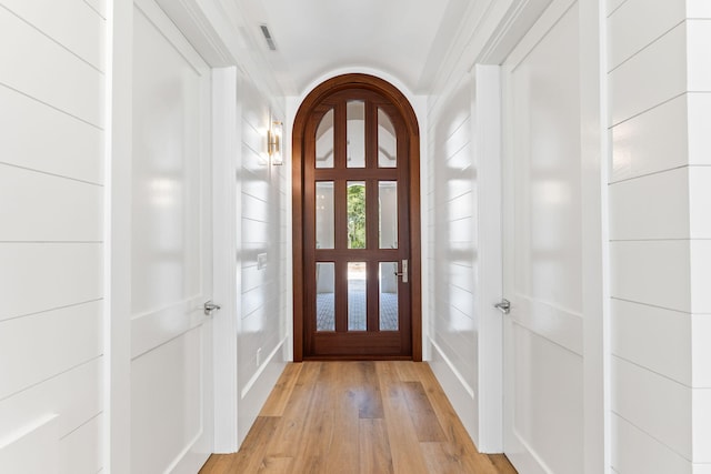 foyer entrance featuring arched walkways, light wood finished floors, and visible vents