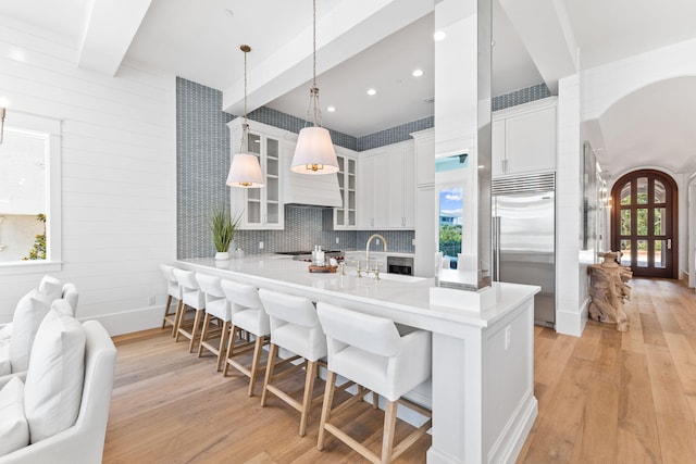 kitchen with white cabinetry, built in fridge, beam ceiling, and light hardwood / wood-style flooring