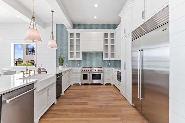 kitchen featuring tasteful backsplash, light hardwood / wood-style floors, hanging light fixtures, built in appliances, and sink