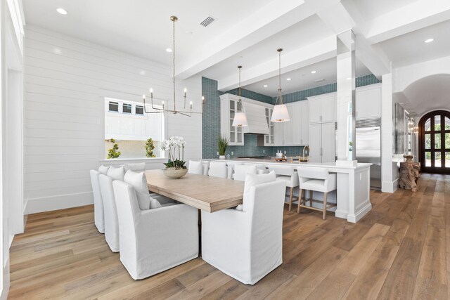 dining space with a notable chandelier, sink, beam ceiling, and light wood-type flooring