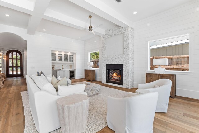 living room featuring beam ceiling, a fireplace, light hardwood / wood-style flooring, and ceiling fan