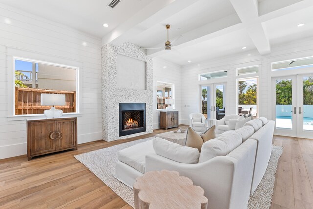 living room with french doors, light hardwood / wood-style flooring, ceiling fan, beamed ceiling, and a fireplace