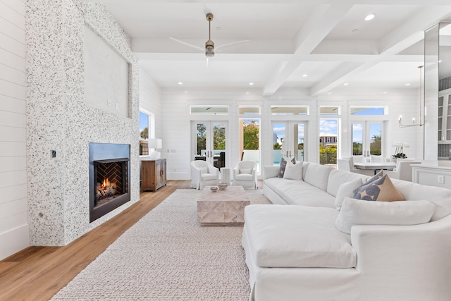 living room featuring light hardwood / wood-style flooring, a fireplace, french doors, beam ceiling, and ceiling fan