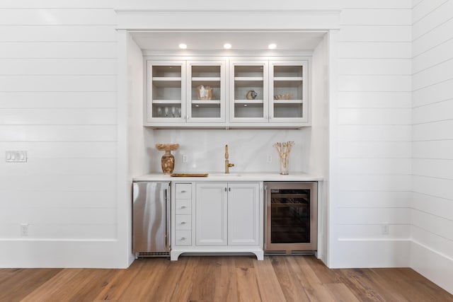 bar featuring freestanding refrigerator, a sink, wood finished floors, beverage cooler, and bar