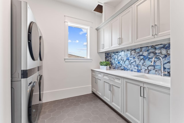 washroom featuring cabinet space, stacked washer / dryer, a sink, tile patterned flooring, and baseboards