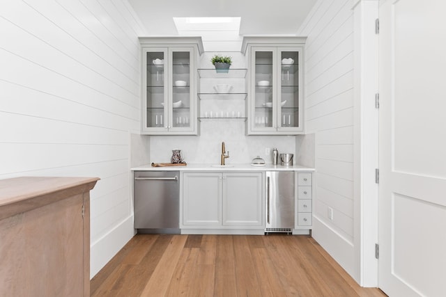 bar with a skylight, light hardwood / wood-style flooring, dishwasher, and gray cabinets