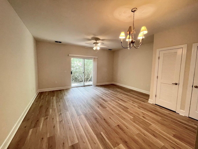 spare room featuring wood-type flooring and ceiling fan with notable chandelier