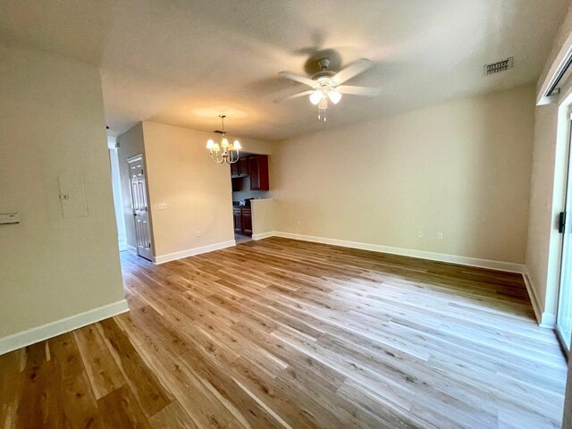 unfurnished living room with light wood-type flooring and ceiling fan with notable chandelier