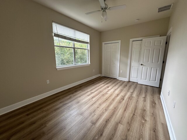 unfurnished bedroom featuring two closets, light hardwood / wood-style floors, and ceiling fan