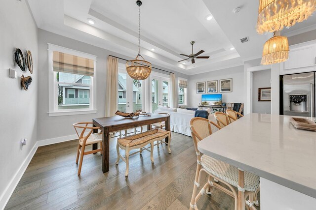 dining space with ceiling fan with notable chandelier, hardwood / wood-style flooring, and a raised ceiling