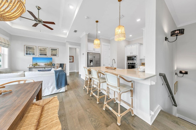 kitchen with a breakfast bar area, light hardwood / wood-style flooring, appliances with stainless steel finishes, ceiling fan, and white cabinets