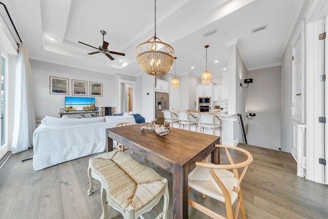 dining area with crown molding, a raised ceiling, ceiling fan with notable chandelier, and light hardwood / wood-style floors