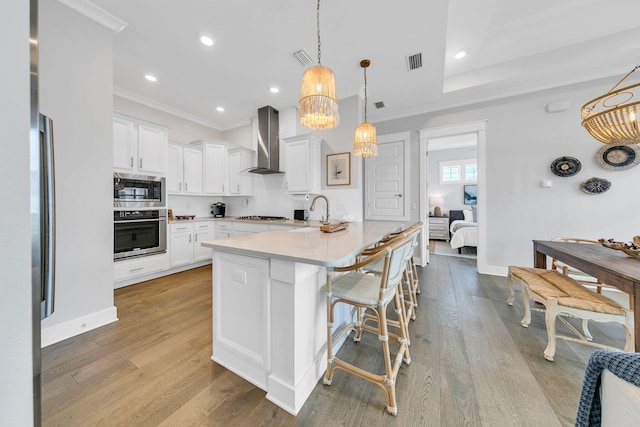 kitchen with wall chimney range hood, white cabinets, stainless steel appliances, and a breakfast bar