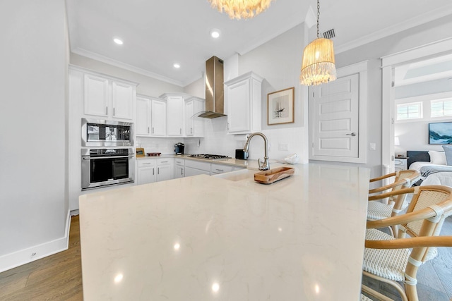 kitchen with pendant lighting, a breakfast bar area, appliances with stainless steel finishes, white cabinetry, and wall chimney exhaust hood