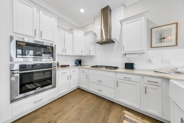 kitchen with ornamental molding, white cabinetry, stainless steel appliances, dark hardwood / wood-style floors, and wall chimney range hood