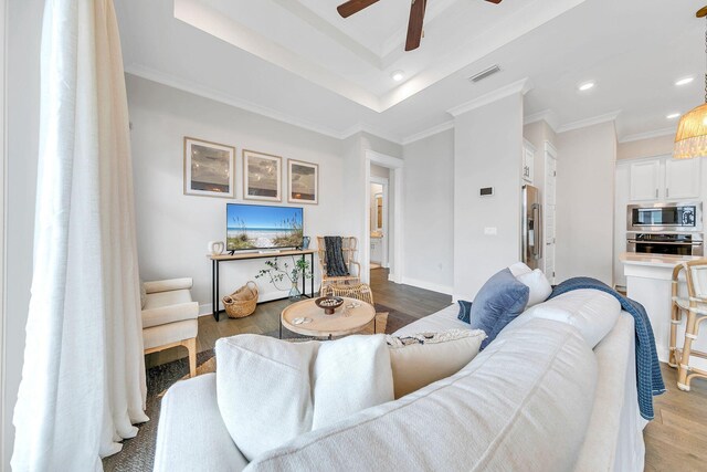 living room with light hardwood / wood-style flooring, ornamental molding, a raised ceiling, and ceiling fan