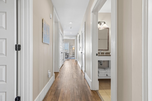 hallway featuring recessed lighting, a sink, baseboards, and wood finished floors