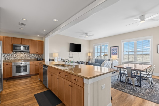 kitchen featuring appliances with stainless steel finishes, an island with sink, ceiling fan, sink, and light hardwood / wood-style floors