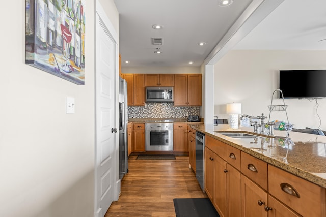 kitchen featuring hardwood / wood-style floors, light stone countertops, backsplash, stainless steel appliances, and sink