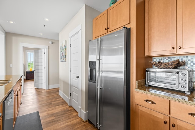 kitchen featuring a toaster, wood finished floors, dark stone counters, appliances with stainless steel finishes, and backsplash