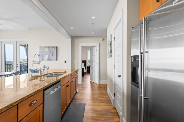 kitchen featuring a sink, light stone countertops, appliances with stainless steel finishes, brown cabinets, and wood finished floors