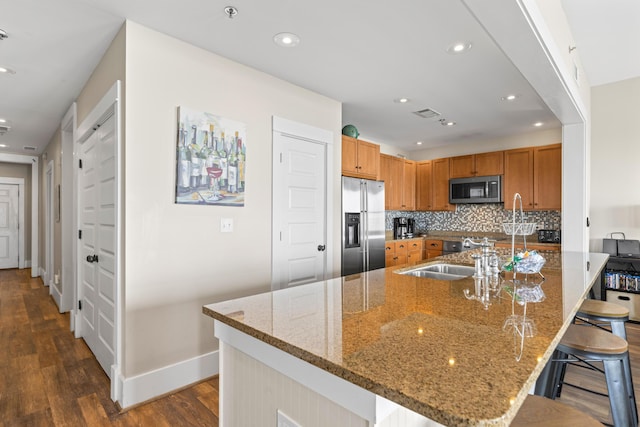 kitchen with a kitchen breakfast bar, tasteful backsplash, stainless steel appliances, a sink, and dark wood-style floors
