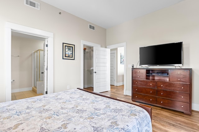 bedroom with baseboards, visible vents, a walk in closet, and wood finished floors