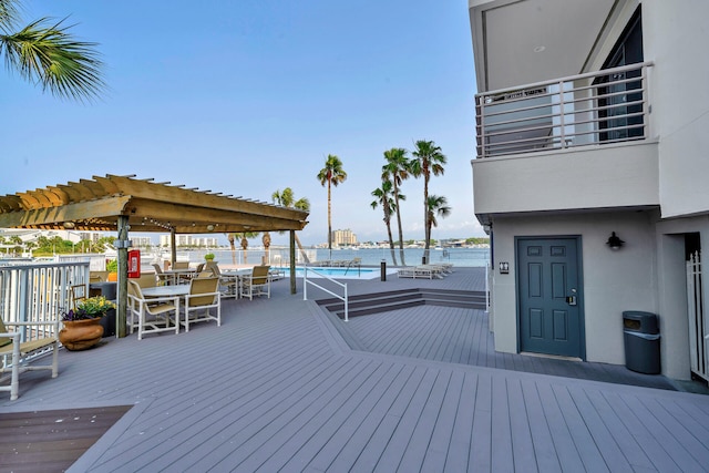 wooden terrace featuring a water view, a community pool, and a pergola