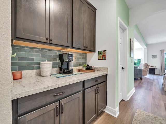 kitchen with backsplash, light hardwood / wood-style floors, dark brown cabinetry, and light stone countertops