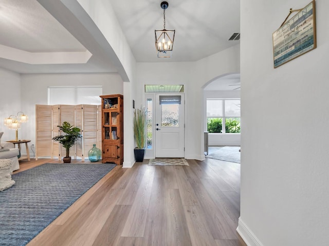 foyer with a raised ceiling, an inviting chandelier, and wood-type flooring