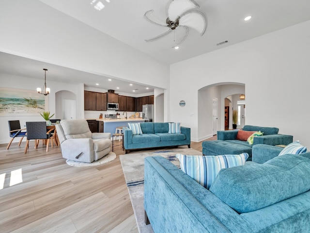 living room with ceiling fan with notable chandelier and light wood-type flooring