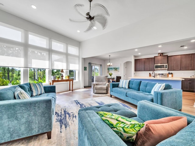 living room with ceiling fan with notable chandelier, light hardwood / wood-style flooring, and a healthy amount of sunlight