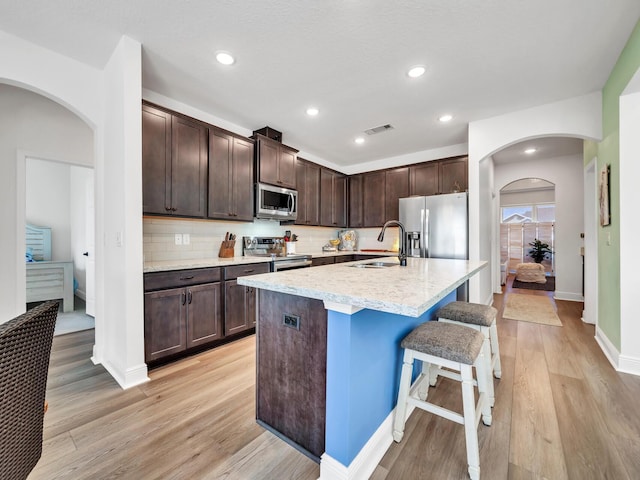 kitchen with light wood-type flooring, tasteful backsplash, sink, stainless steel appliances, and dark brown cabinets