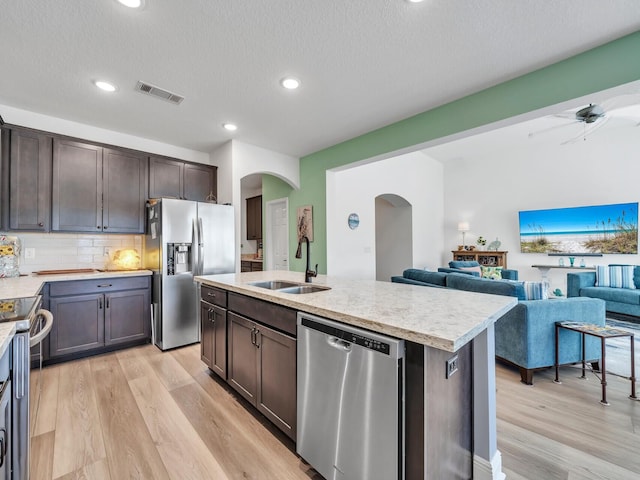 kitchen with appliances with stainless steel finishes, backsplash, sink, an island with sink, and light wood-type flooring