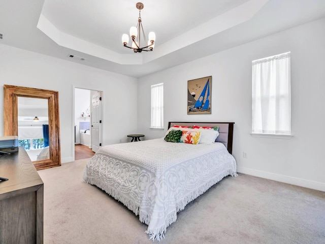 carpeted bedroom with connected bathroom, a tray ceiling, and a chandelier