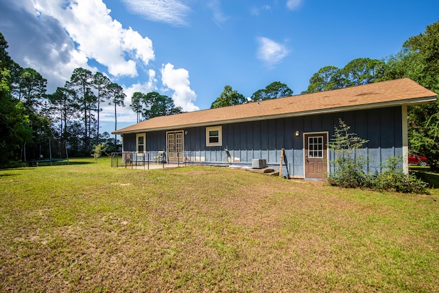 back of house with a lawn, a trampoline, and central air condition unit