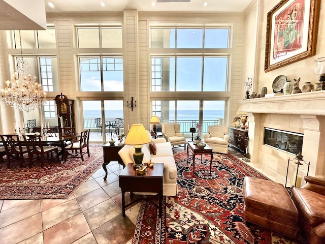 tiled living room with plenty of natural light, a high ceiling, a chandelier, and a water view