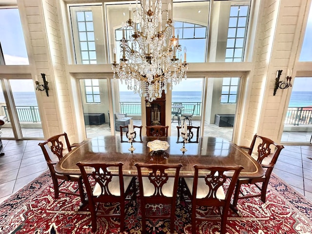 tiled dining area featuring a water view, a towering ceiling, and an inviting chandelier