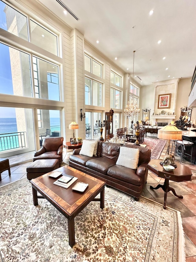 tiled living room with a chandelier, a water view, a towering ceiling, and plenty of natural light