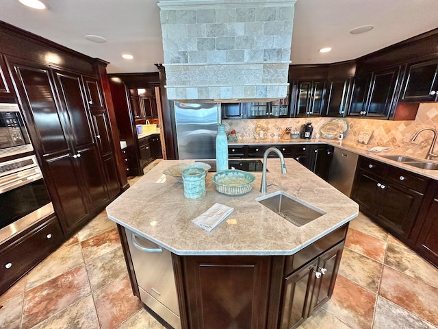 kitchen featuring appliances with stainless steel finishes, sink, an island with sink, light stone counters, and decorative backsplash