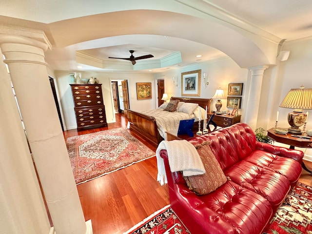 bedroom with hardwood / wood-style floors, ceiling fan, a raised ceiling, ornate columns, and crown molding