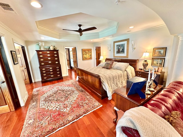 bedroom featuring ornamental molding, wood-type flooring, a raised ceiling, and ceiling fan