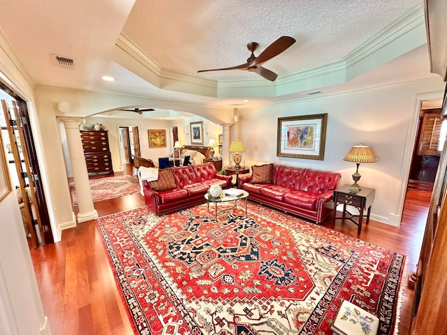 living room featuring ornamental molding, ceiling fan, ornate columns, and a raised ceiling