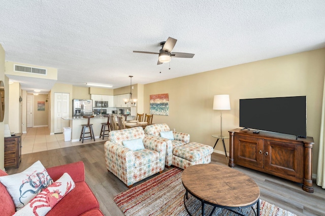 living room featuring ceiling fan with notable chandelier, a textured ceiling, and light wood-type flooring