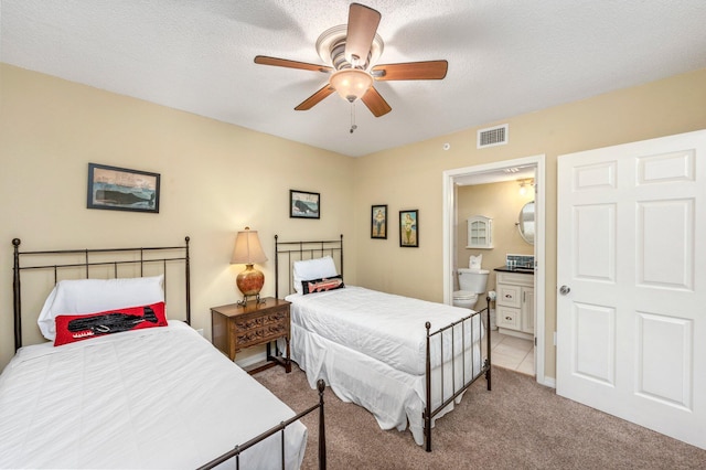 bedroom with ceiling fan, a textured ceiling, ensuite bathroom, and light carpet