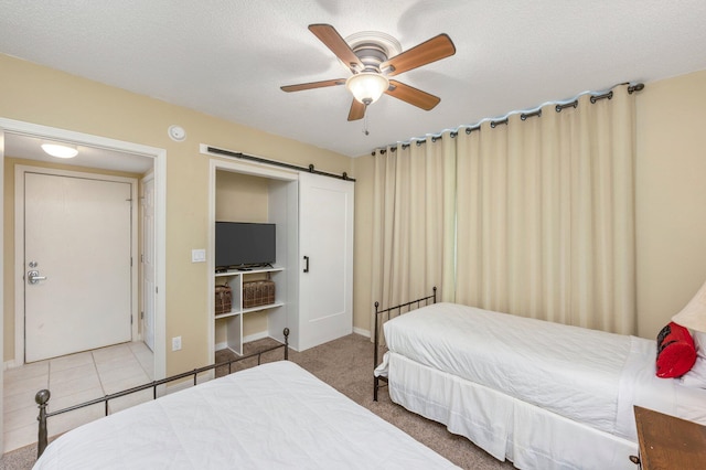 bedroom featuring ceiling fan, a barn door, light colored carpet, and a textured ceiling