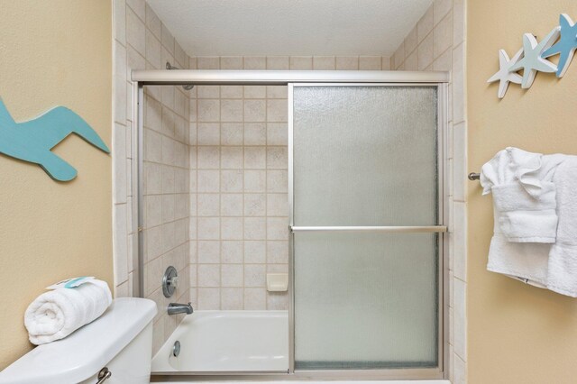 bathroom with enclosed tub / shower combo, a textured ceiling, and toilet